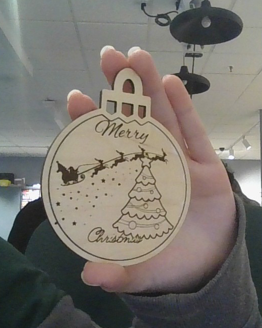 Real finished wooden holiday ornament held in a classroom, with a cut outline, hanging hole, and engraved seasonal artwork